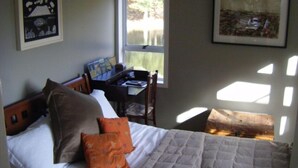 Une chambre à coucher avec un lit, des oreillers, un bureau et une chaise. Une fenêtre laisse entrer la lumière naturelle.