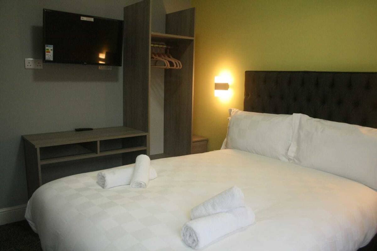 Quarto de hotel com cama, televisão na parede, mesa de cabeceira, cómoda e guarda-roupa.