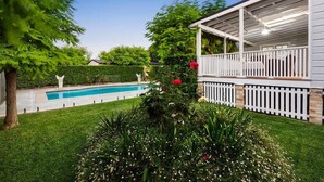 A house with a covered porch, a swimming pool, and a well-maintained garden.