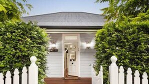 A house with a white picket gate, a dark pathway leading to the entrance, and a well-maintained lawn.