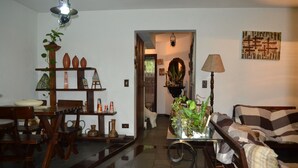 Un salon comprenant un canapé, une table basse et un coin repas avec des chaises et une table. On y trouve une plante posée sur un support et une lampe sur une table d’appoint.