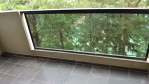 Une pièce dotée d’une grande fenêtre donnant sur une forêt dense. La pièce a un sol carrelé et un mur blanc.