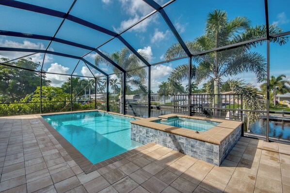 Zona de piscina con un jacuzzi, rodeada de paredes de vidrio y palmeras.