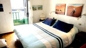 Un dormitorio con cama, almohadas, mesita de noche, lámpara y una obra de arte en la pared.