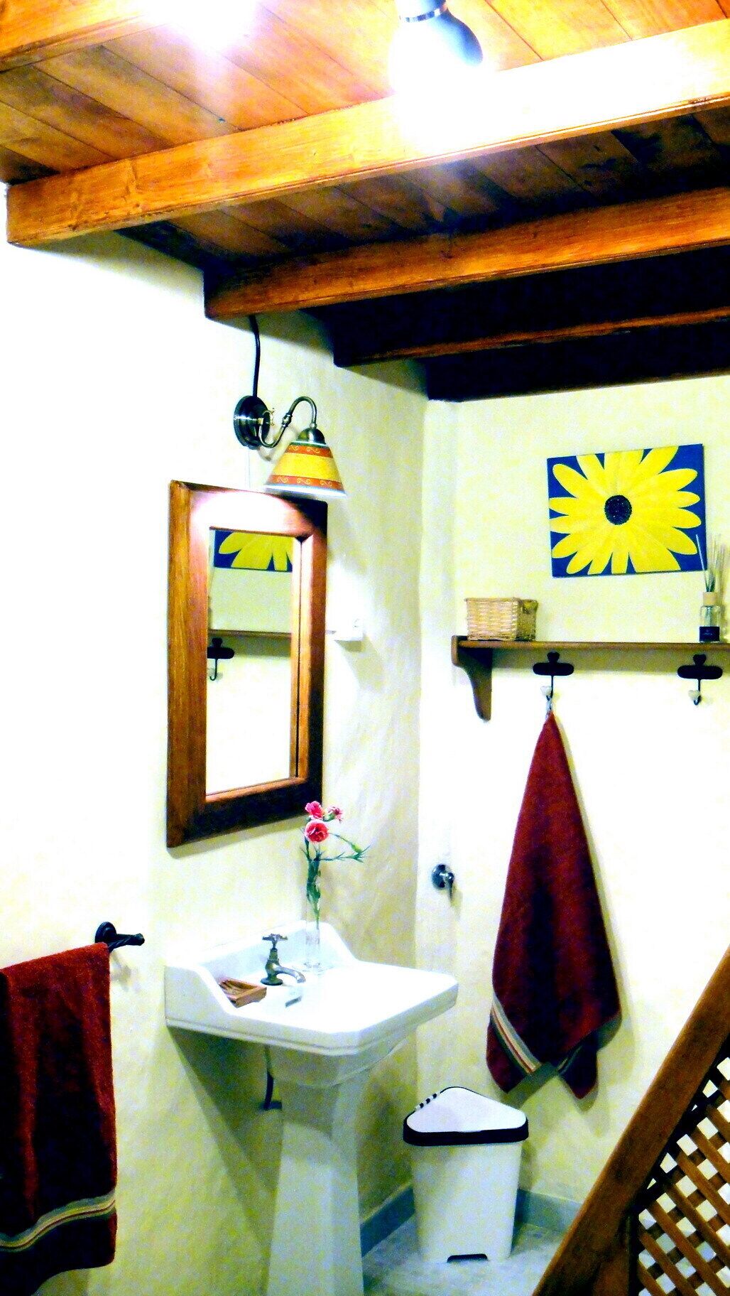 Ein Badezimmer mit Holzboden, einem weißen Waschbecken, einem Spiegel, einem roten Handtuch und einem an der Wand befestigten Regal mit Korb.