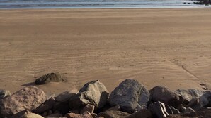 Une plage avec un rivage rocheux et une mer calme sous un ciel partiellement nuageux.