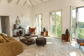 A spacious living room with a herringbone floor, a brown sofa, a wooden coffee table, and a large window offering a view of greenery. - Villa Agni, Contemporary villa in excellent location just 200 meters from Agni Beach (Agni Beach)