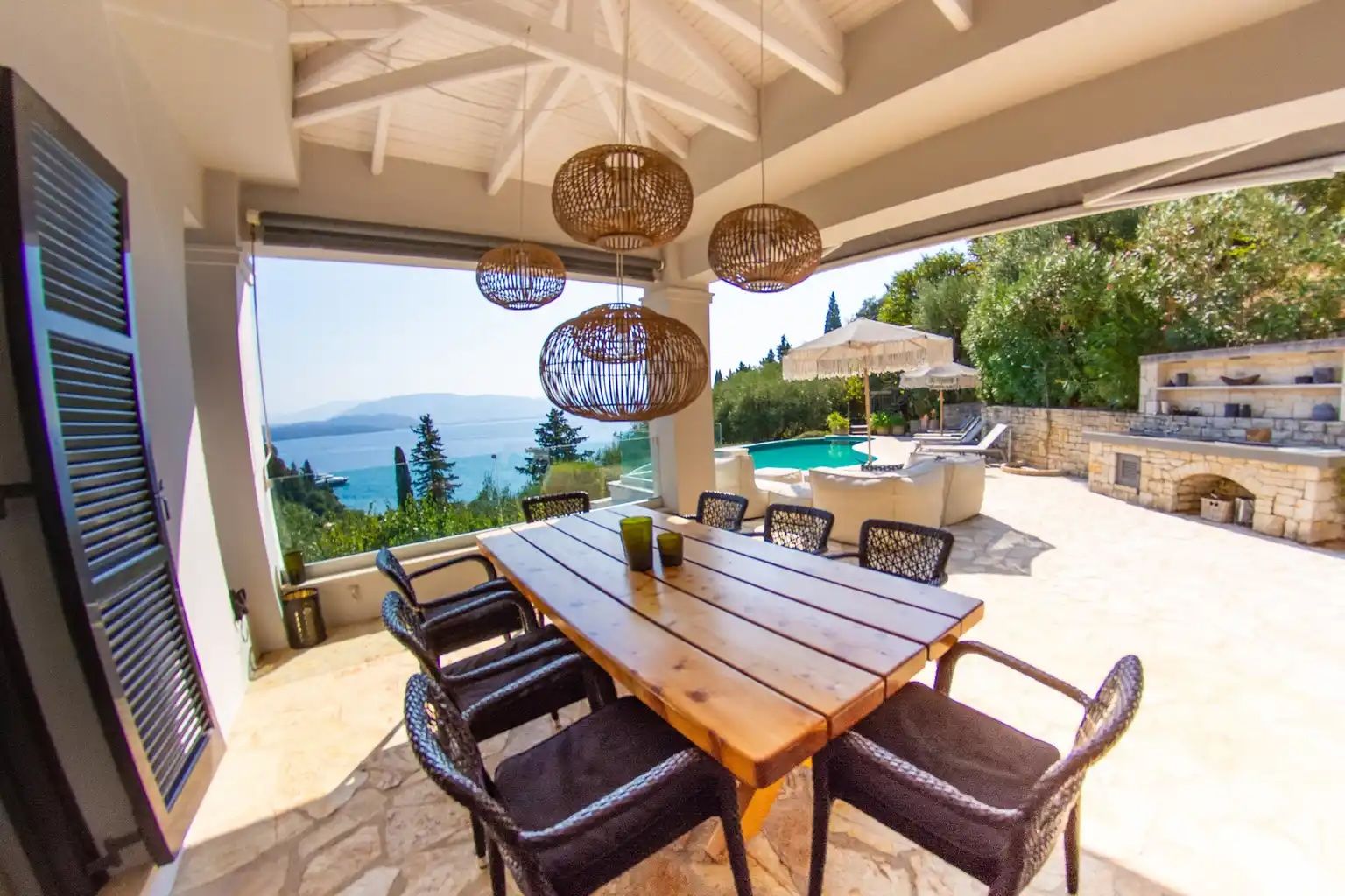 A dining area with a table and chairs, a view of the sea, and outdoor seating with umbrellas.