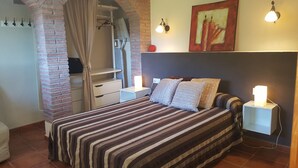 A bedroom with a striped bedspread, a headboard, two bedside lamps, a nightstand, a wardrobe, and a brick wall. - Blanes: beautiful house with pool and garden (Blanes)