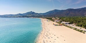 Une plage aux eaux turquoise et limpides, un rivage sablonneux et, en toile de fond, des montagnes.