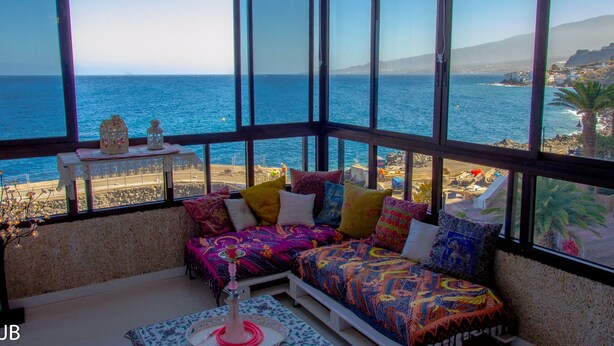 A balcony with a view of the sea, a sofa with colorful cushions, and a small table with decorative items. - Apartment in 1 sea line (tabaiba)