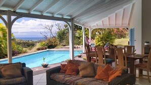 Un espacio al aire libre techado con piscina, muebles de mimbre y una mesa de comedor.