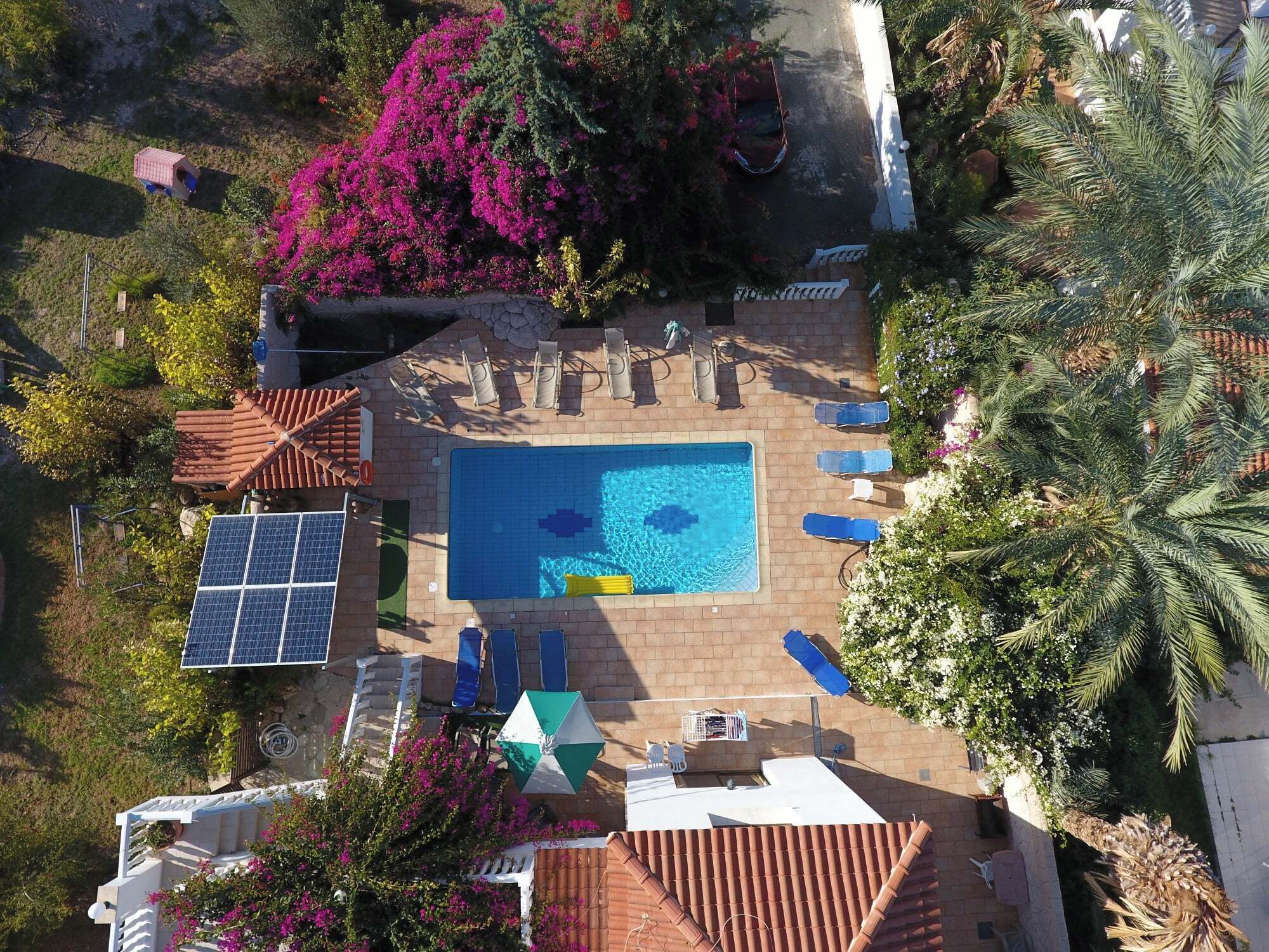 Vue aérienne d’un espace piscine aménagé sur un toit, avec une piscine, des chaises longues et un petit bâtiment doté d’un toit rouge.