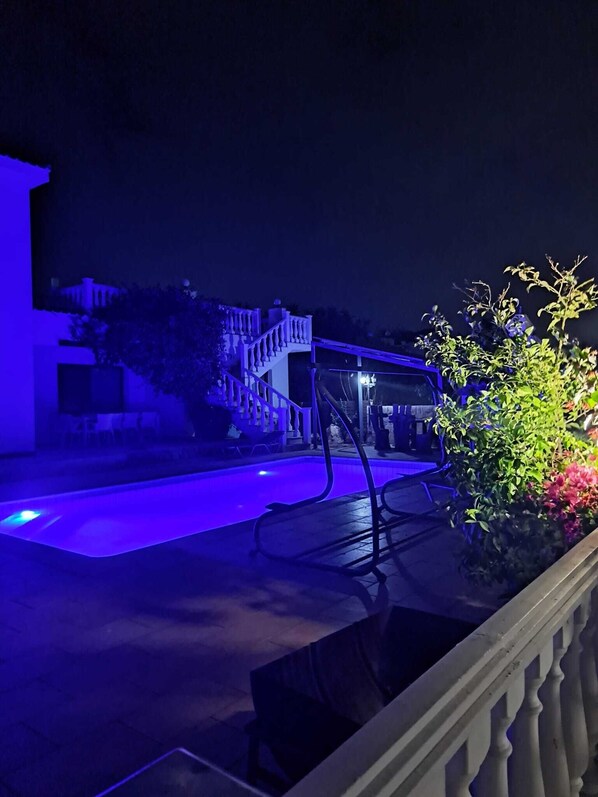 Vista nocturna de una zona de piscina con una escalera que lleva a un edificio.