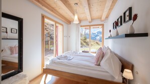 A bedroom with a wooden ceiling, a large bed, a mirror, and a view of mountains. - Chalet Wyssbirg (Wengen)