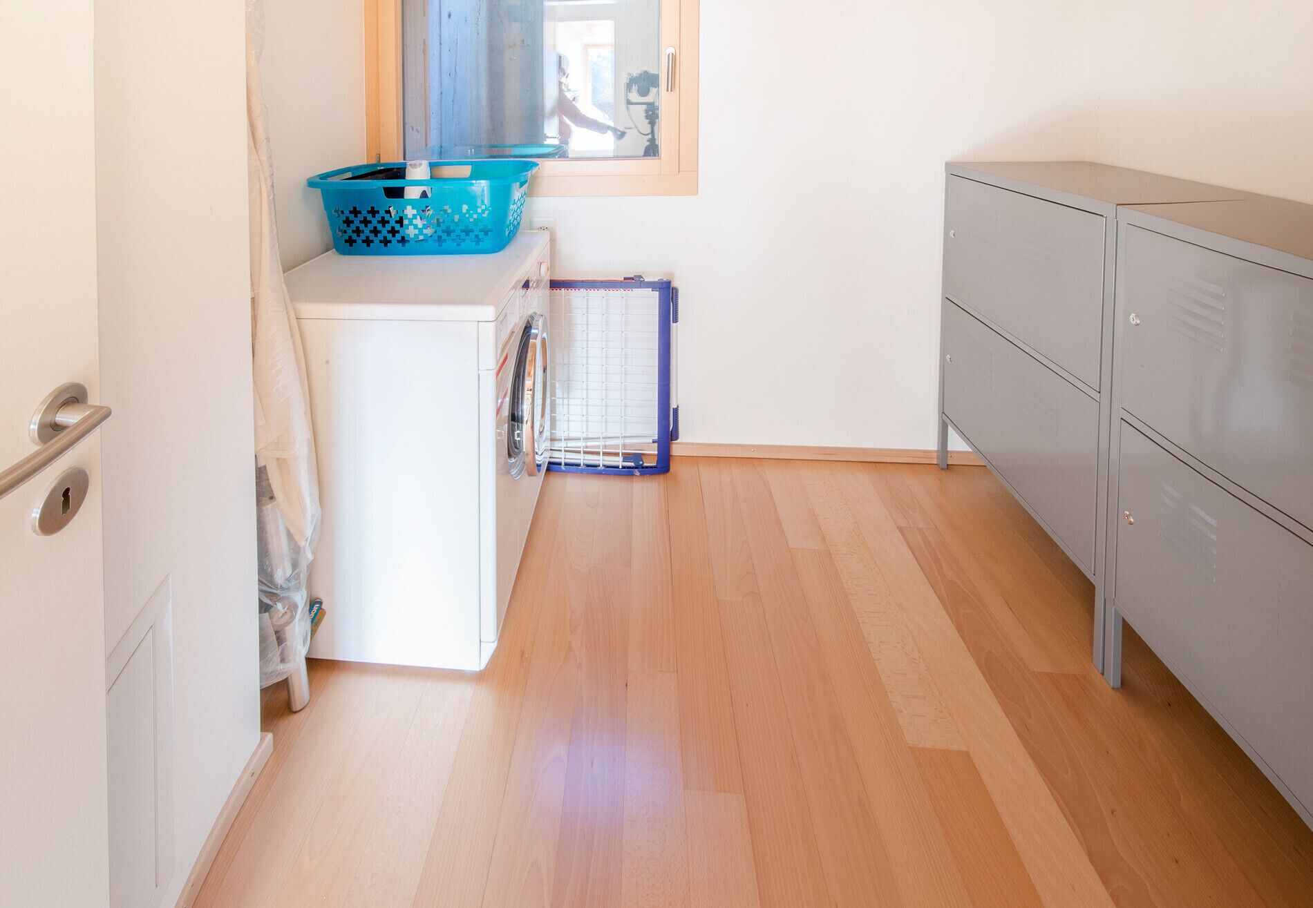 Eine kleine Küche mit Waschmaschine, Wäscheständer und einem grauen Schrank.