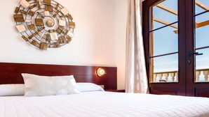 Habitación de hotel con una cama grande, un adorno en la pared, una ventana con vistas y un cabecero de madera.