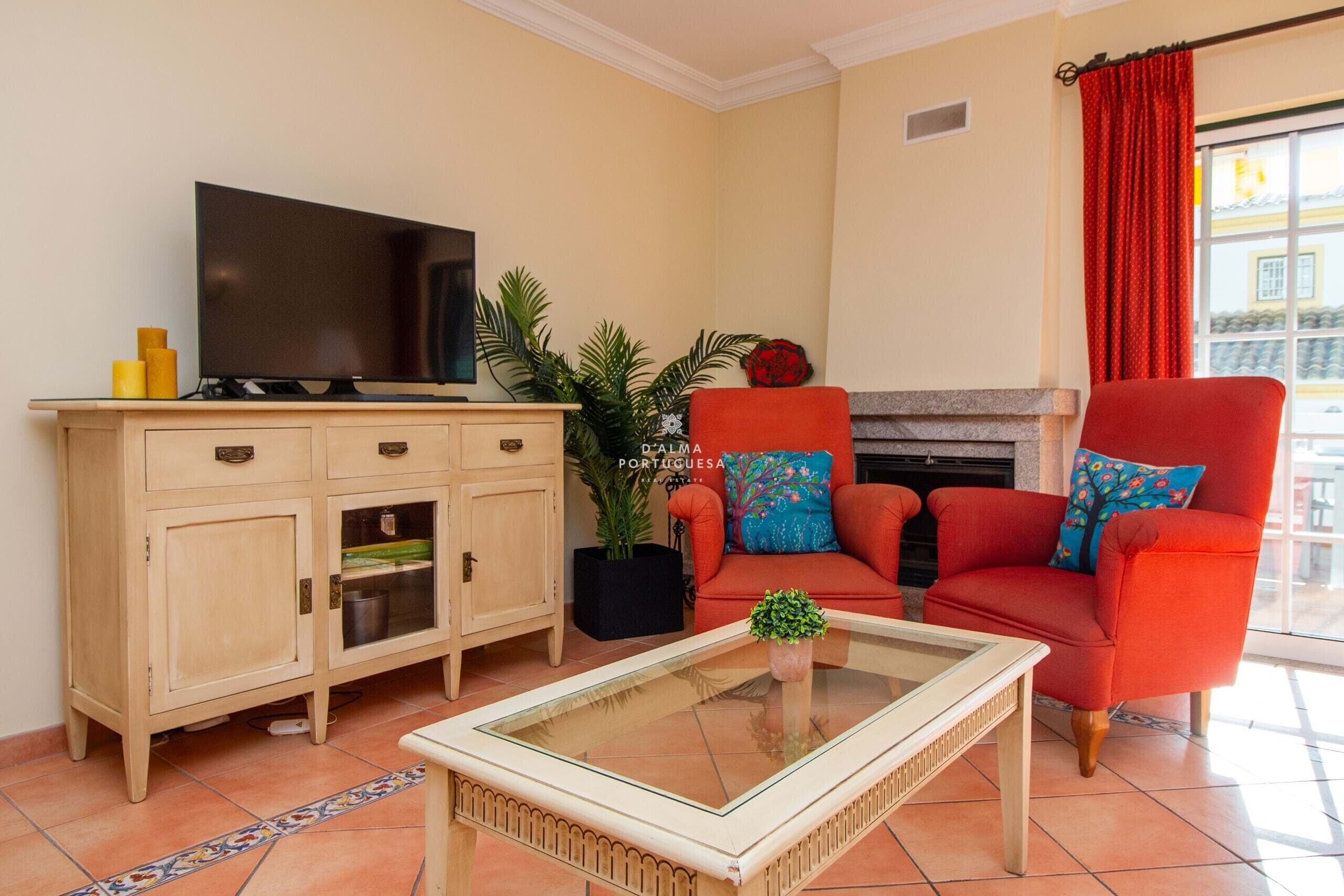 Een woonkamer met een televisie, een bank, een salontafel, een kast en een open haard.