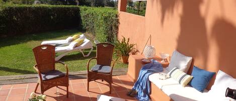 Eine sonnendurchflutete Terrasse mit einer Couch, zwei Korbstühlen, einem kleinen Tisch und einer Liege.