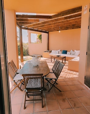 Une terrasse extérieure avec une table et des chaises en bois, un canapé et une structure en forme de pergola.