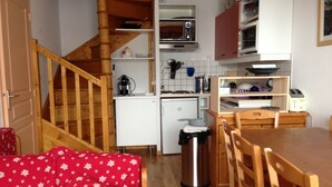 Une cuisine compacte avec un escalier en bois, un coin repas avec une table et des chaises, et une petite poubelle.