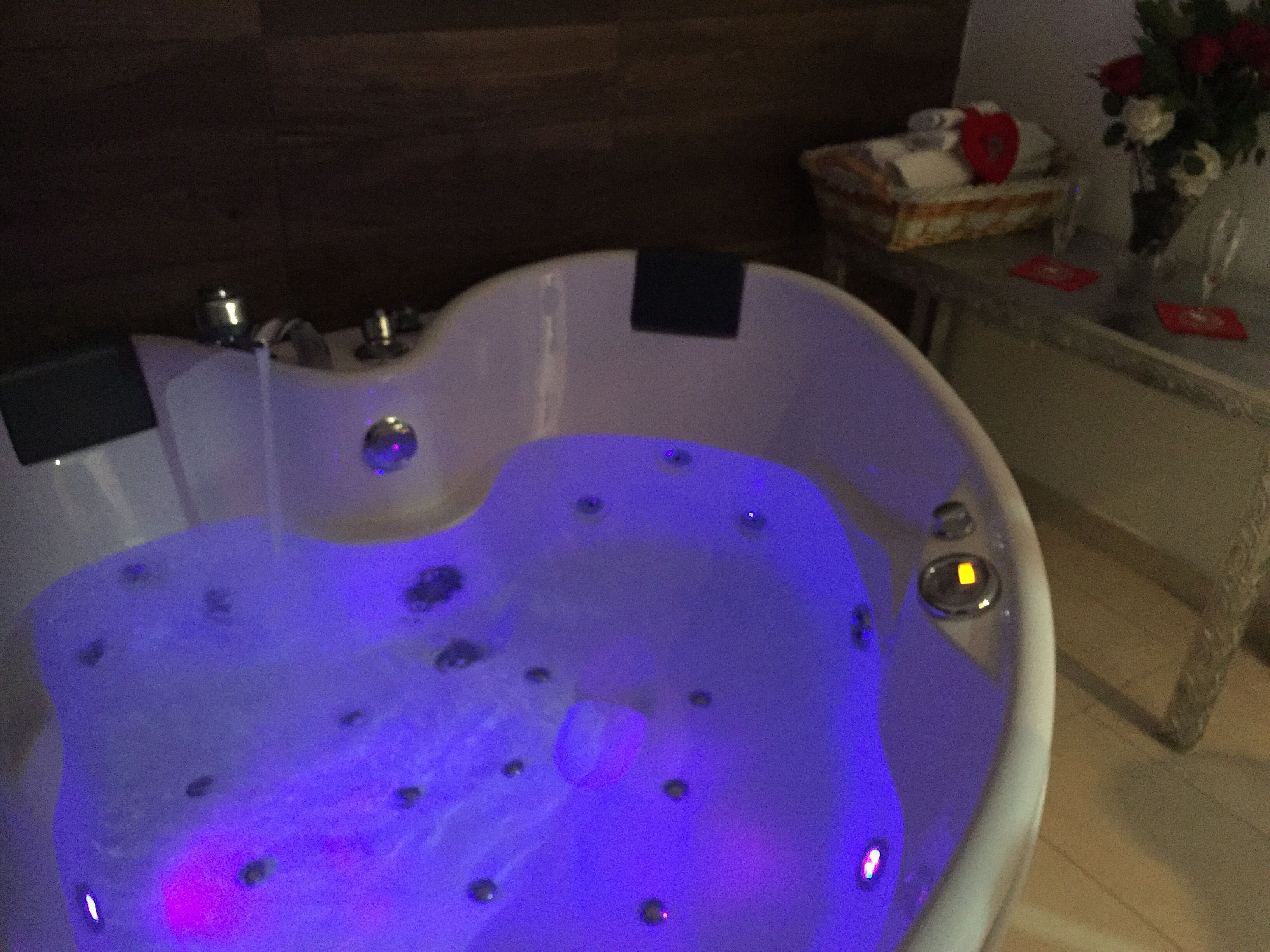 A hot tub with water jets, a control panel, and a small table with a vase of flowers.
