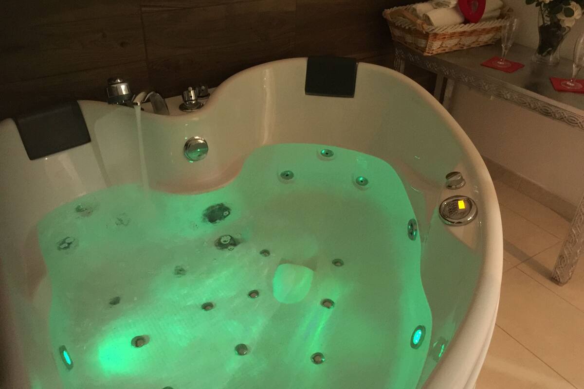 Una bañera con jets de hidromasaje, una pared de madera, y una mesa con una cesta y flores.