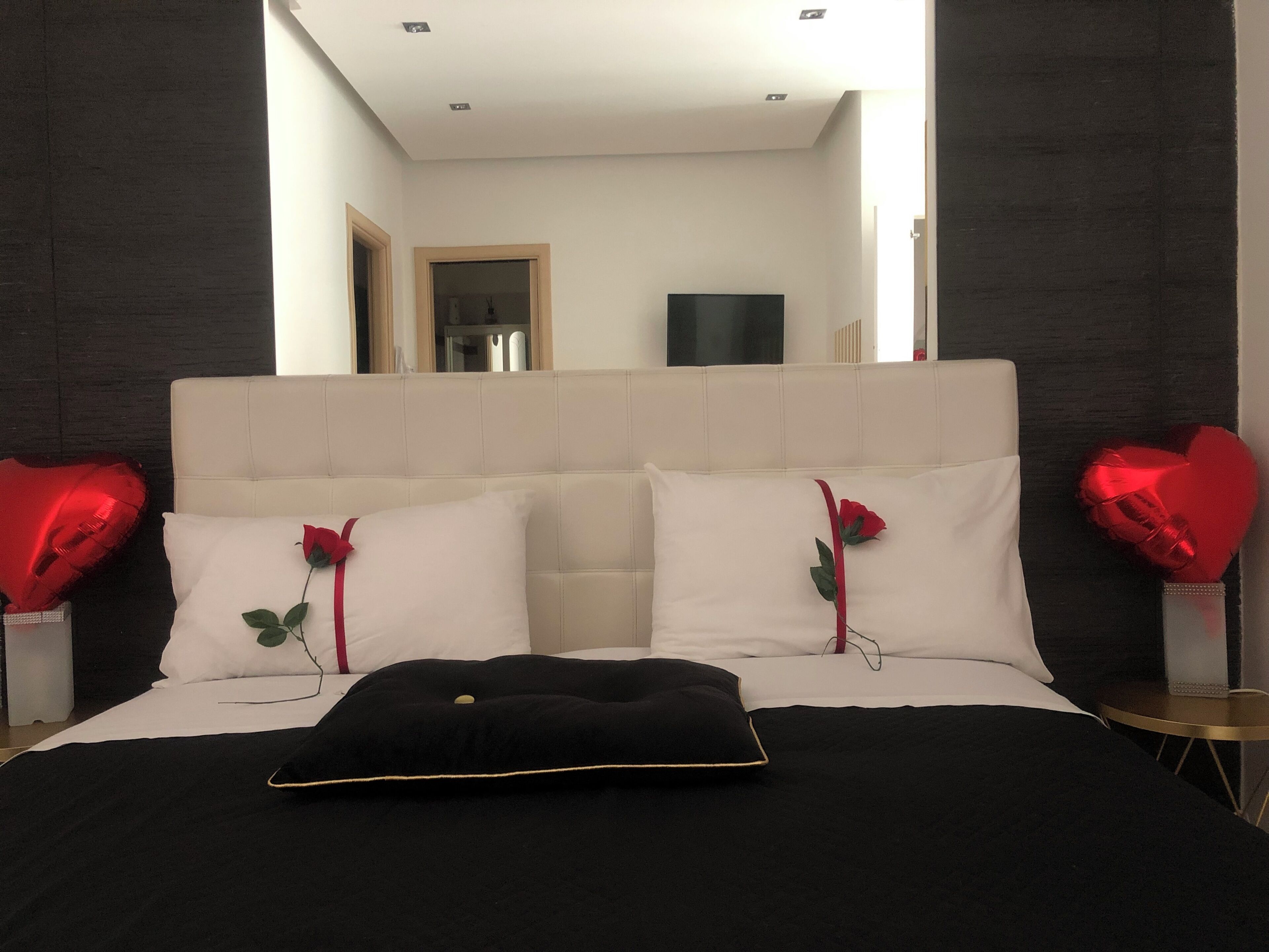 A bed with white and black bedding, two heart-shaped pillows, and a black pillow with a gold trim.