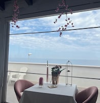 Ein Tisch mit Kerze, Glas und Blumen auf einem Balkon mit Meerblick.