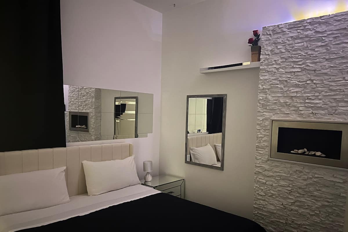 Una habitación de hotel moderna con una cama, una mesita de noche, un espejo y una pared con textura de piedra.