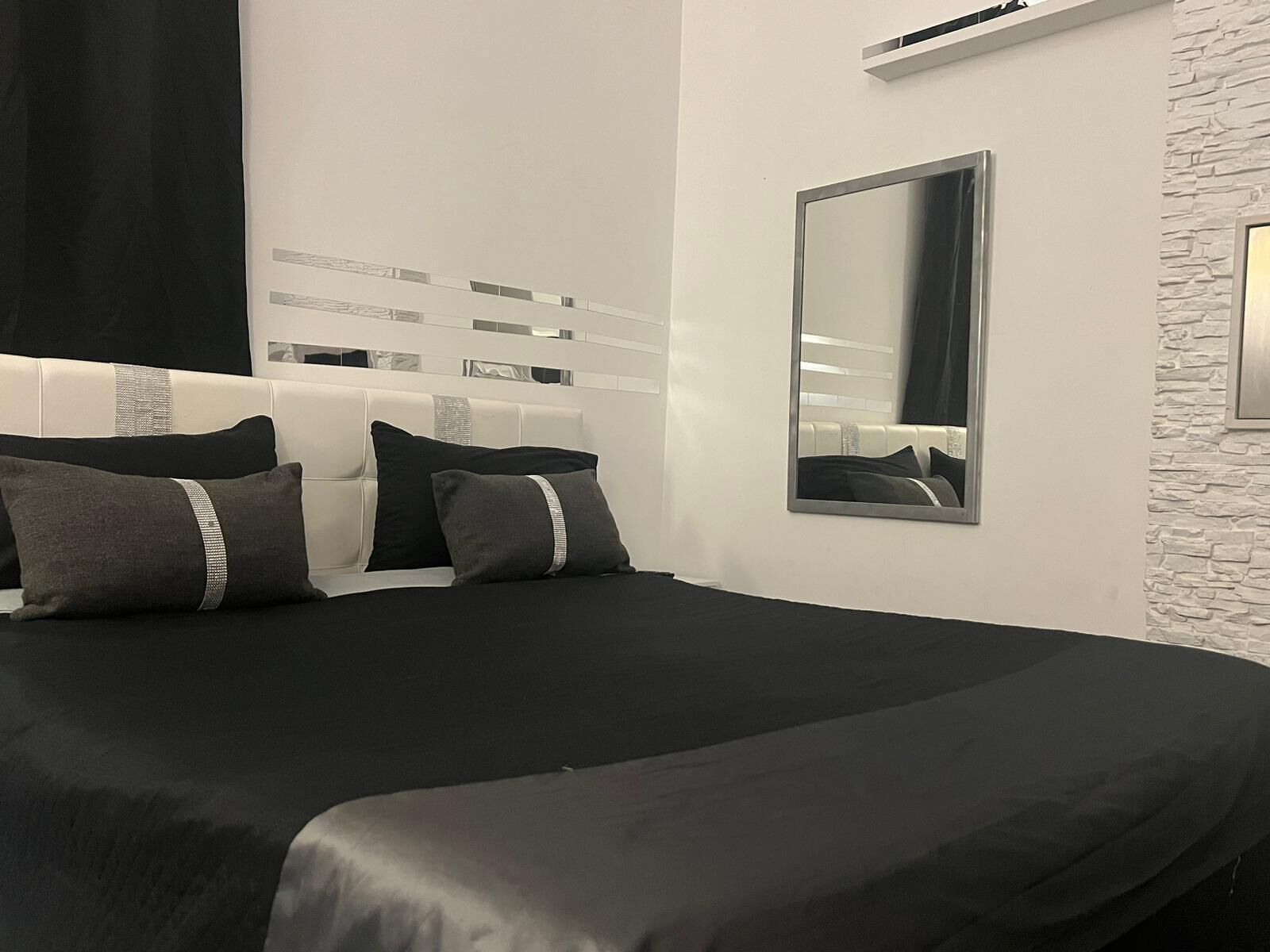 Una camera da letto moderna con un letto grande, uno specchio e un muro bianco con texture.