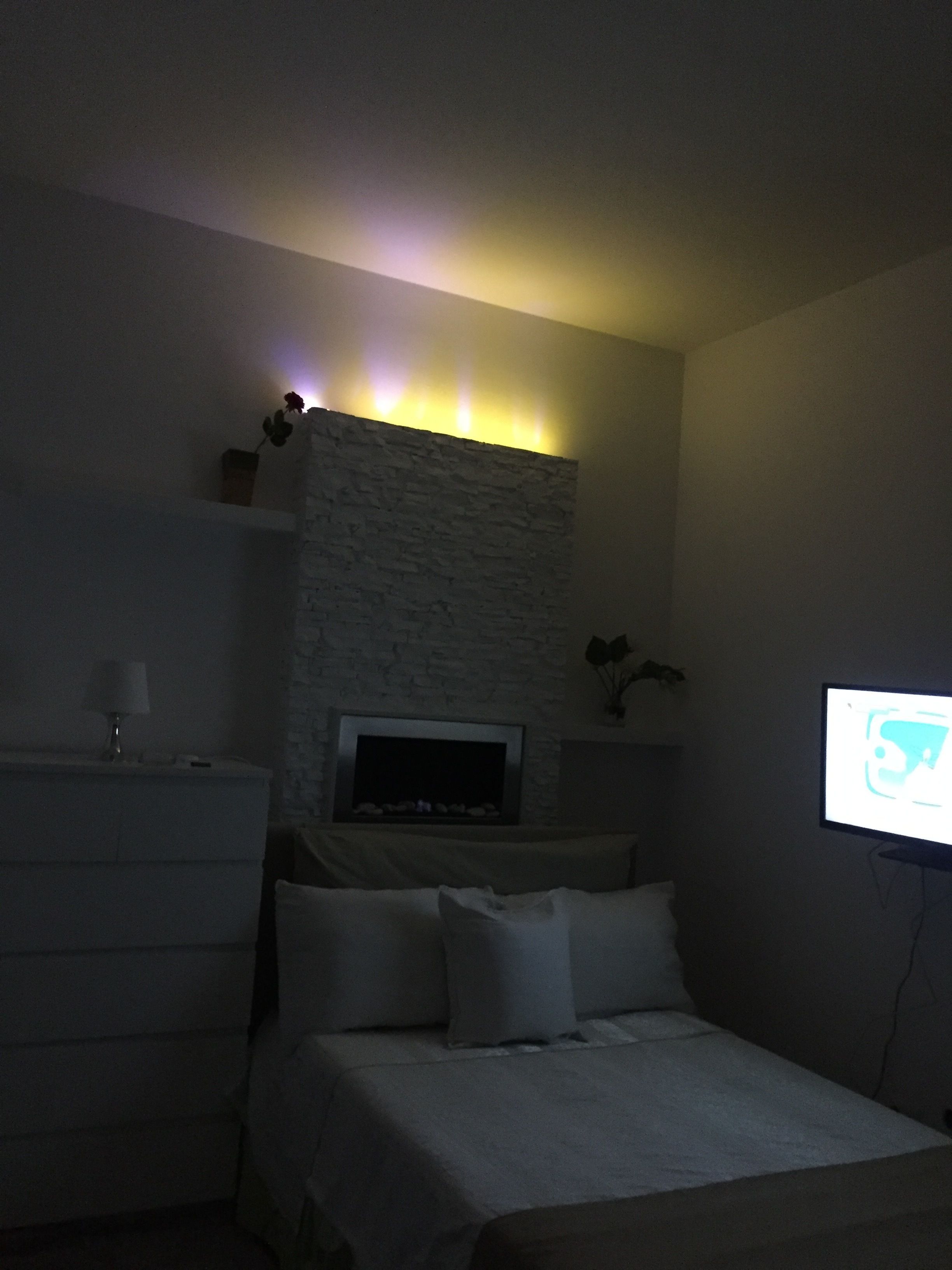 Una habitación de hotel tenuemente iluminada con una cama, un televisor y una pared de piedra.