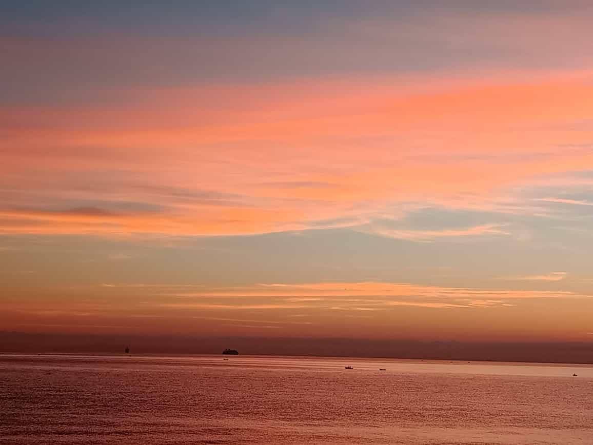 A sunset over a calm sea with a distant ship and a small boat.