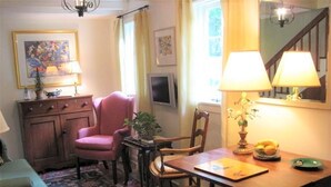 Et hyggeligt værelse med skrivebord i træ, en lyserød stol, en bænk og et spisebord med en lampe.