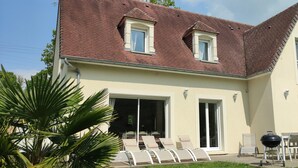 Ein zweigeschossiges Haus mit einem geneigten Dach, einem Balkon und einer Terrasse mit Gartenmöbeln.