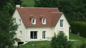 Ein zweistöckiges Haus mit geneigtem Dach, einer Veranda und einem kleinen Vorgarten.