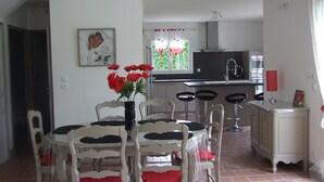 Ein Essbereich mit Tisch und Stühlen, im Hintergrund eine Küche und ein Fenster mit Vorhängen.