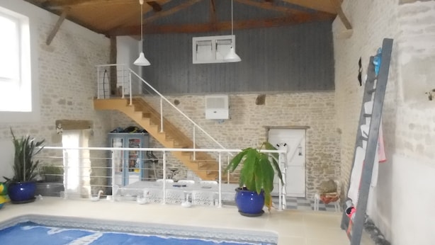 Un vaste espace intérieur abritant une piscine, accessible par un escalier menant à un niveau supérieur, et entouré de murs en pierre et de poutres en bois.