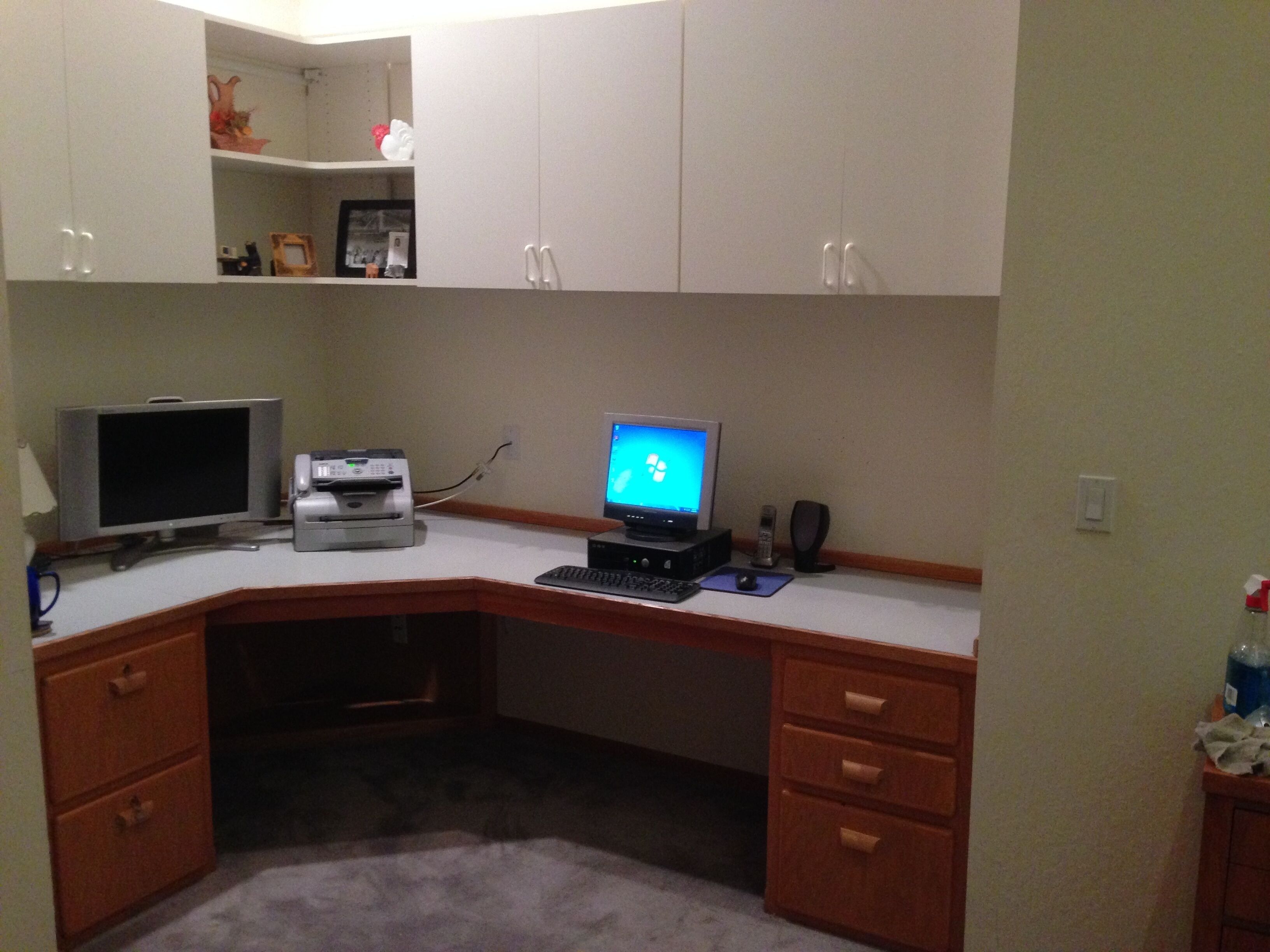 A corner office with a desk, two monitors, a printer, and a telephone.