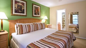 Una habitación de hotel con cama, dos cuadros colgados en la pared, un ventilador de techo y una ventana con cortinas.