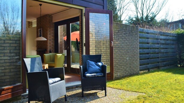 Eine offene Terrasse mit Korbstühlen, einem gelben Sofa und einem Kamin aus Backsteinen.