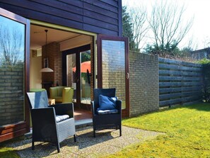 An open patio with wicker chairs, a yellow sofa, and a brick fireplace.