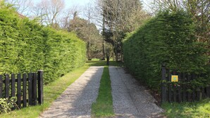 Ein Kiesweg, gesäumt von dichten, grünen Hecken und einem Holzzaun.