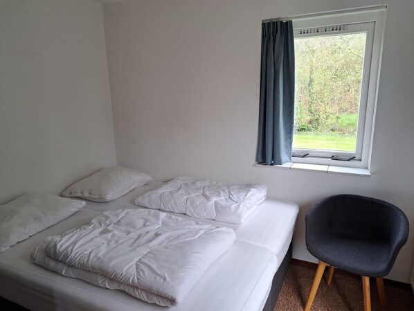 A single bed with white bedding, a grey chair, and a window with curtains.