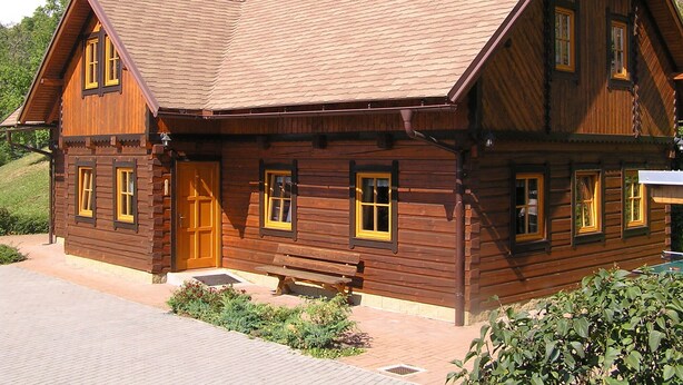 A wooden cabin with a sloped roof, a satellite dish, and a bench outside.