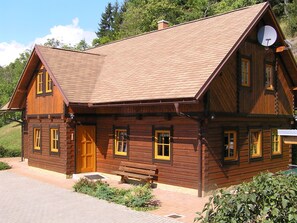 A wooden cabin with a sloped roof, a satellite dish, and a bench outside.