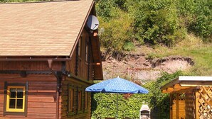 A wooden cabin with a satellite dish, a patio with wooden chairs, and a blue umbrella.