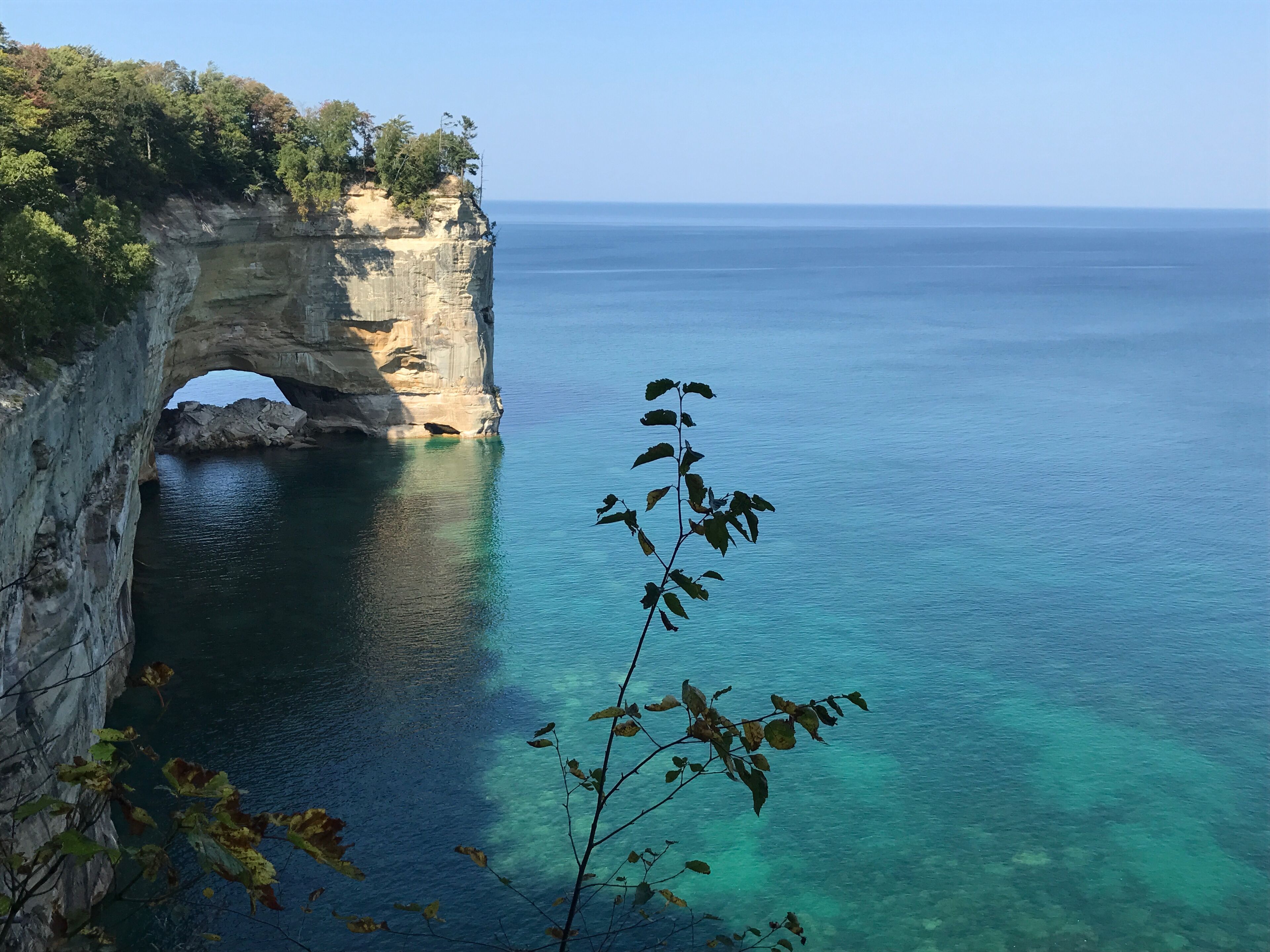 A coastal cliff with a natural arch formation and clear blue waters.
