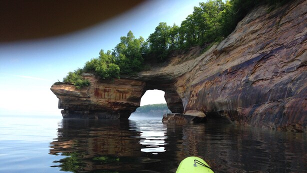 A kayak on calm water with a natural rock arch formation in the background.