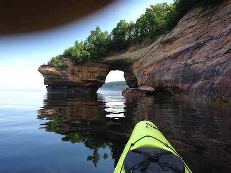 A kayak on calm water with a natural rock arch formation in the background.